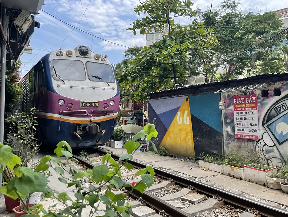 Reunification Express train beside tracks, with a painted wall shown as a symbol of slow travel.