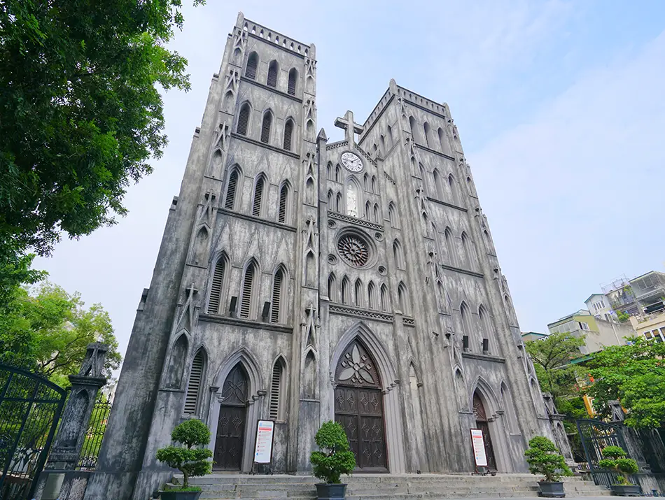 Neo-gothic stone cathedral with twin towers overlooking a lively urban square.