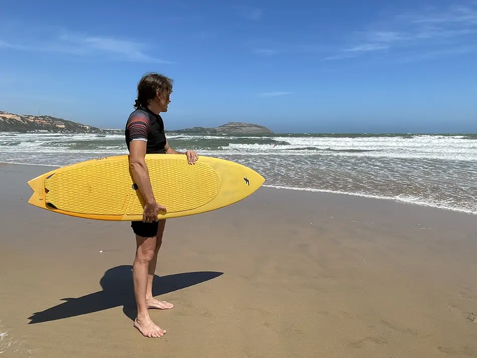 A surfer standing with a yellow surf-board on the beach in Vietnam
