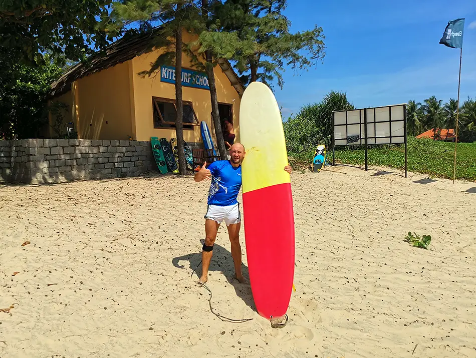 A traveler holding a surfboard on the beach in Mui Ne, showing surfing as one of the things to do in Mui Ne.