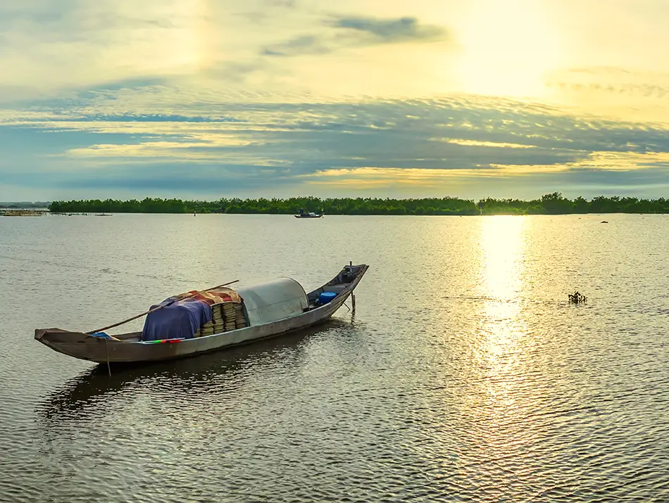 Small wooden fishing boat floating on calm lagoon waters under a soft sunset sky.
