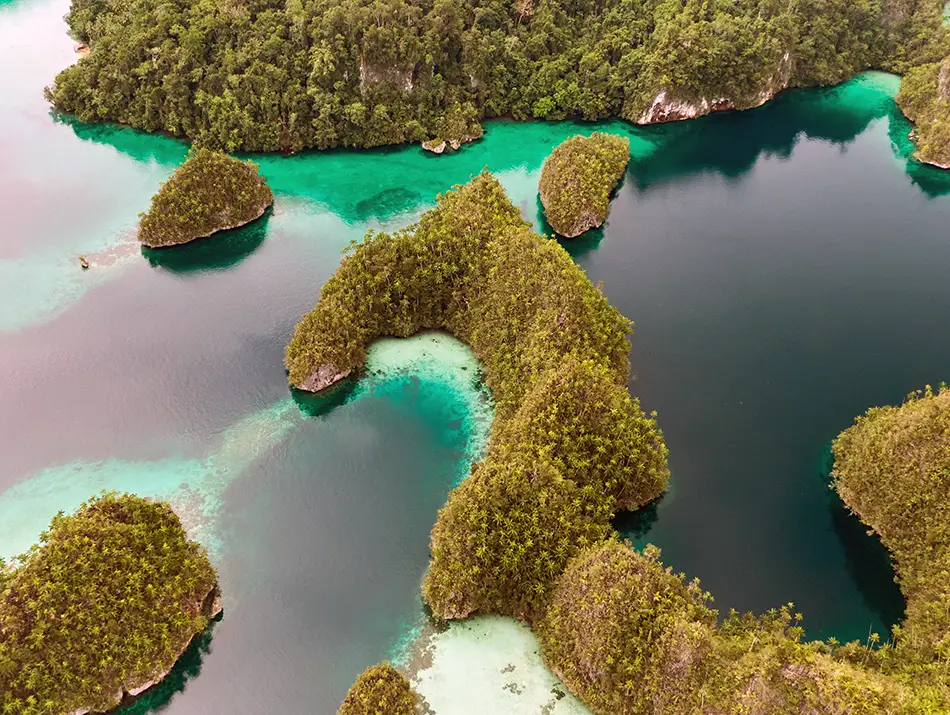 Emerald islets dot a shallow lagoon with teal channels and sand patches.