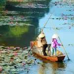 Traditional wooden boat gliding through a lotus-filled river in Vietnam, showing local waterway life and low-impact, nature-based travel.