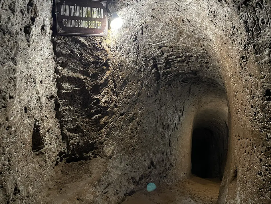 Narrow underground tunnel corridor shows rough concrete walls and low arched ceilings.