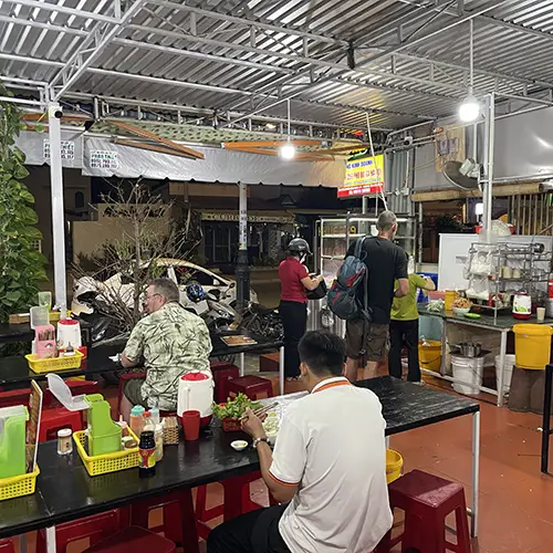 Dining area with plastic chairs and customers eating noodle soup.