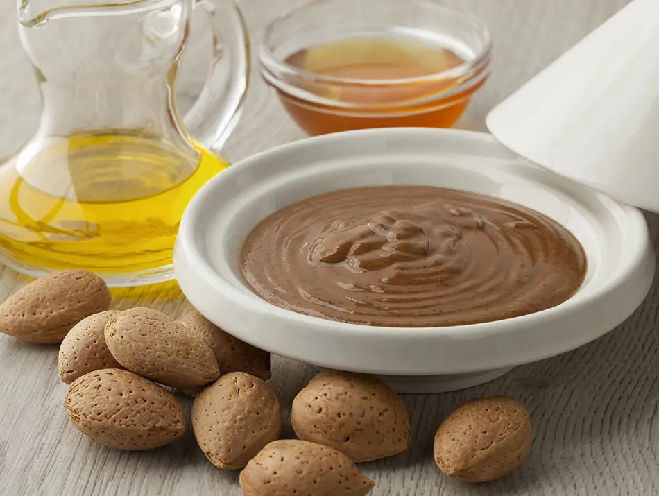 Bowl of amlou dip served with whole almonds and a bottle of argan oil.