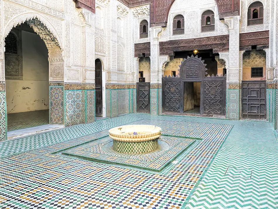 Carved cedarwood and tiled courtyard fountain inside Bou Inania Madrasa in Meknes.