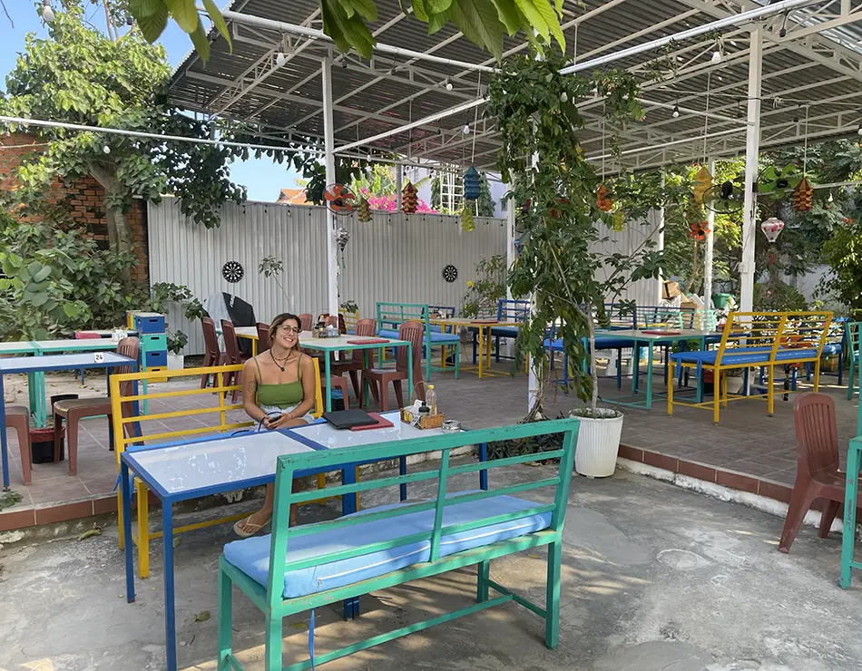 Colorful patio with benches, plants, and string lights under a metal canopy.