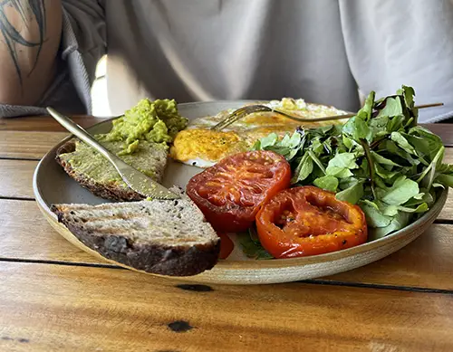 Breakfast plate with toast, grilled tomatoes, greens, and a creamy spread.