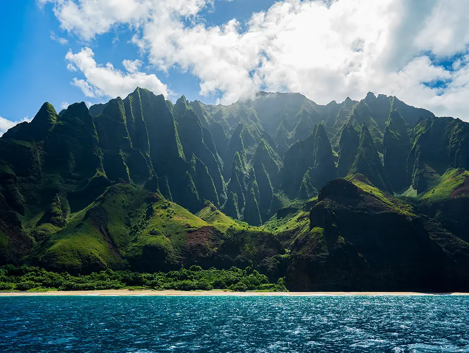 Dramatic Na Pali Coast cliffs rising above turquoise ocean, featured in Jurassic Park.