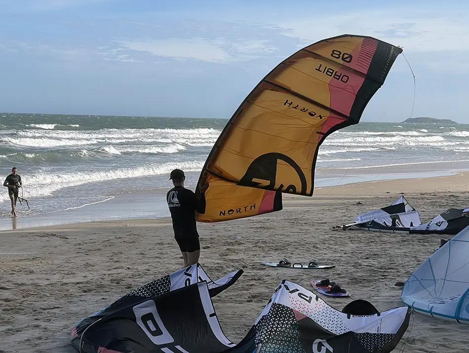 A student launches a yellow kite at the shoreline with instructor nearby,
