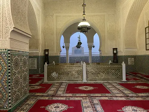 Ornate chamber with marble tombs and tiled arches inside the Meknes mausoleum.