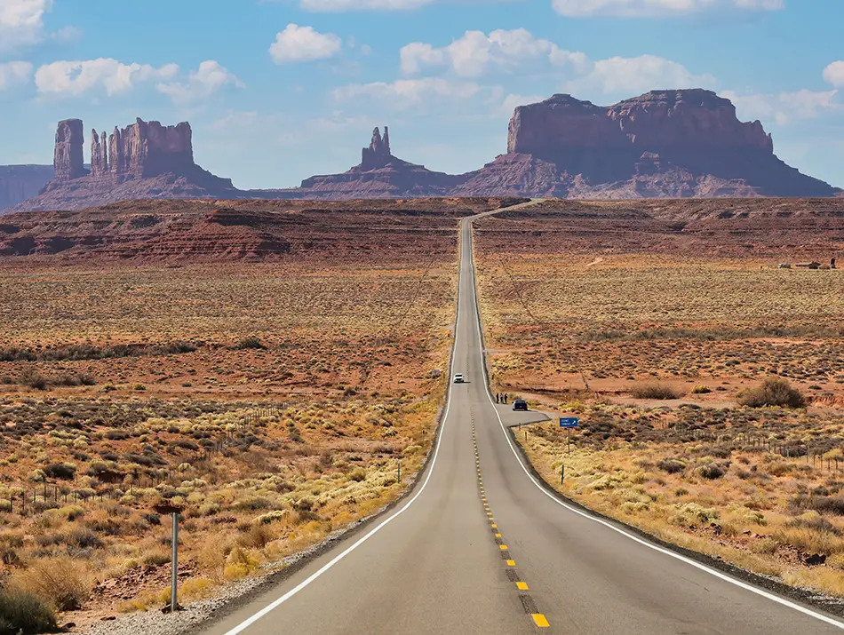 Long desert highway stretching toward towering mesas in Monument Valley, USA.
