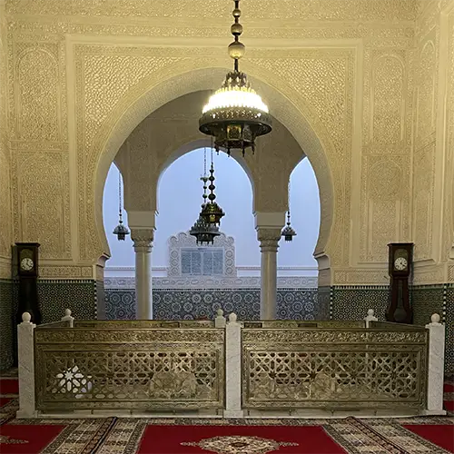 Red carpeted tomb chamber beneath carved arches inside the Moulay Ismail mausoleum.