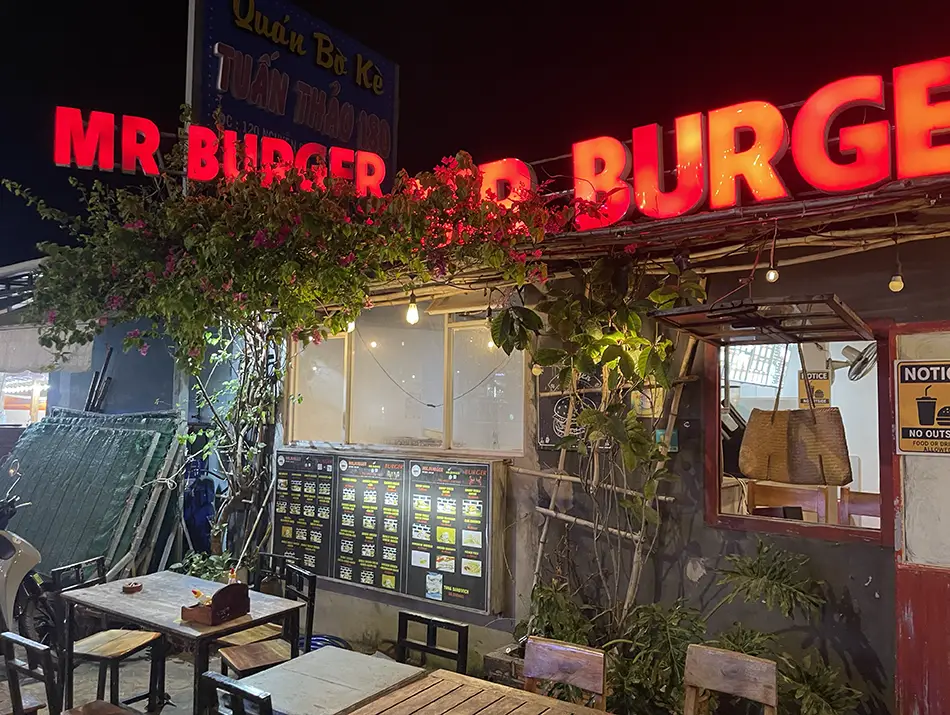 Small storefront with bright signage and outdoor tables after dark.