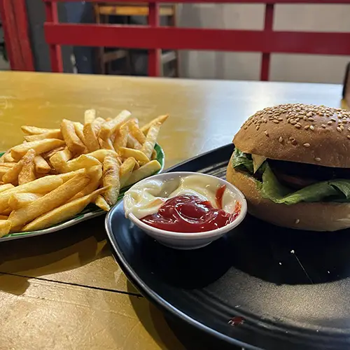 Burger served with fries and dipping sauce on a dark plate.