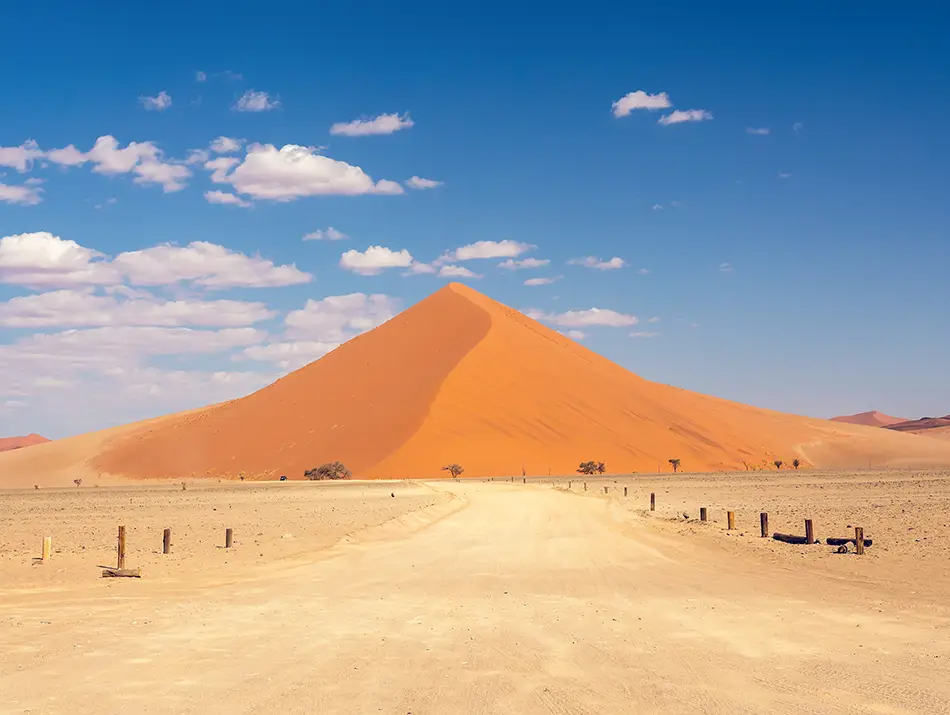 High orange dune rises above a wide desert plain under clear skies.