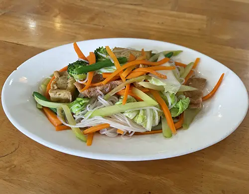 Vegetable salad with shredded carrots, herbs, and peanuts on a white plate.