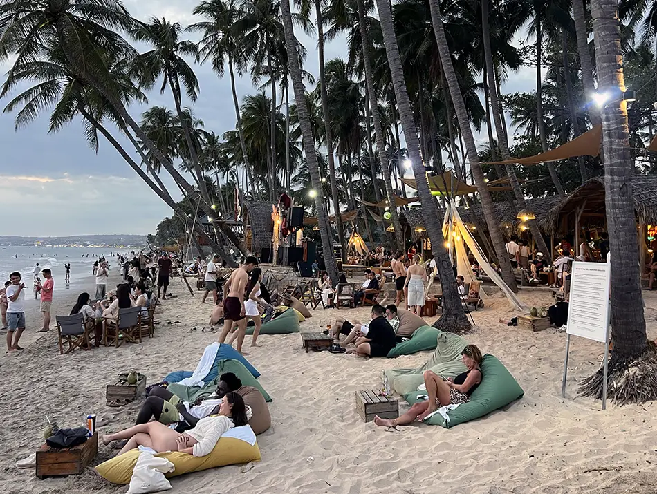 Guests relaxing on the sand under palm trees at a beach bar in mui ne.