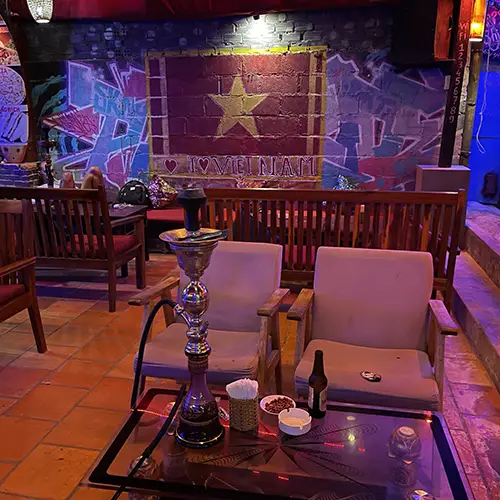 Dimly lit bar interior with tables, chairs, and decorative lighting.