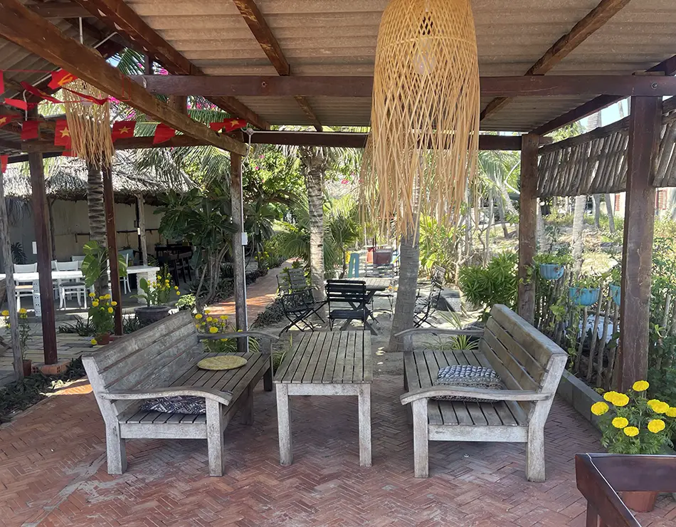 Open-air dining area with wicker chairs, plants, and a large bamboo pendant lamp.