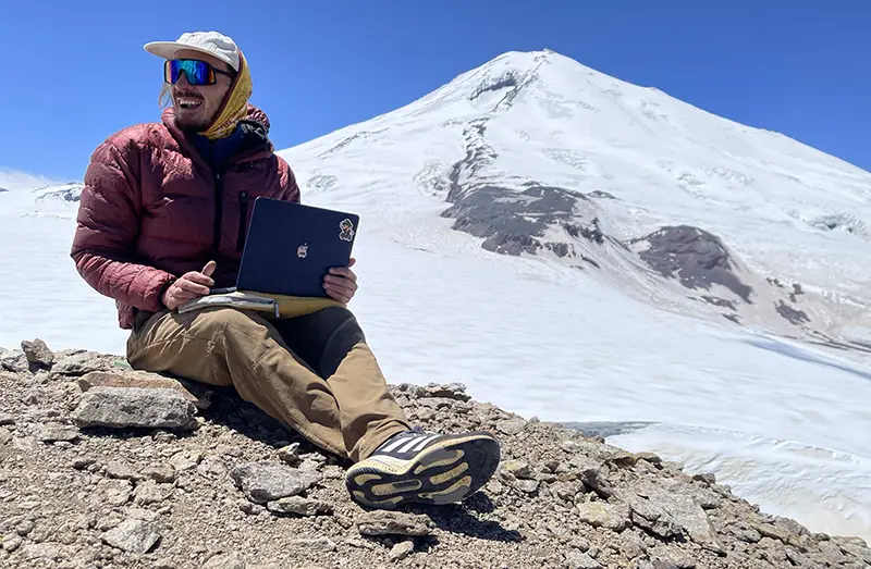 Guides and stories author Yuriy Malykh with laptop in front of mount Elbrus