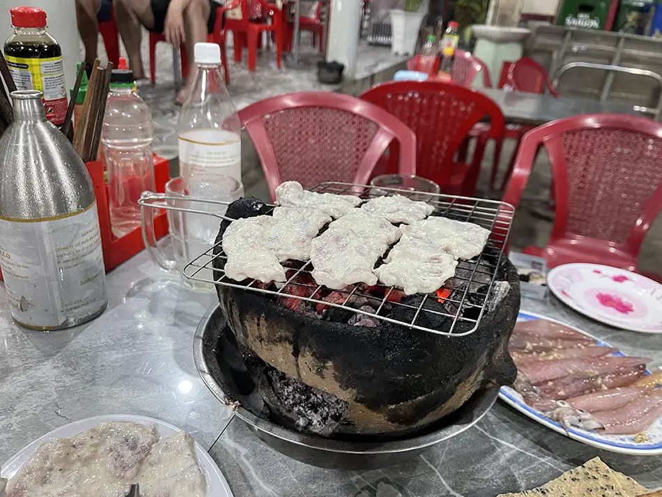 Charcoal grill with skewers and hot pot set on a metal table.