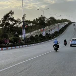 Motorbikes and a car driving along a wide road in Mui Ne lined with trees and streetlights.