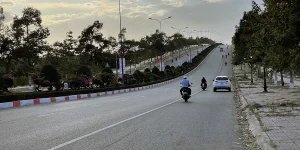 Motorbikes and a car driving along a wide road in Mui Ne lined with trees and streetlights.