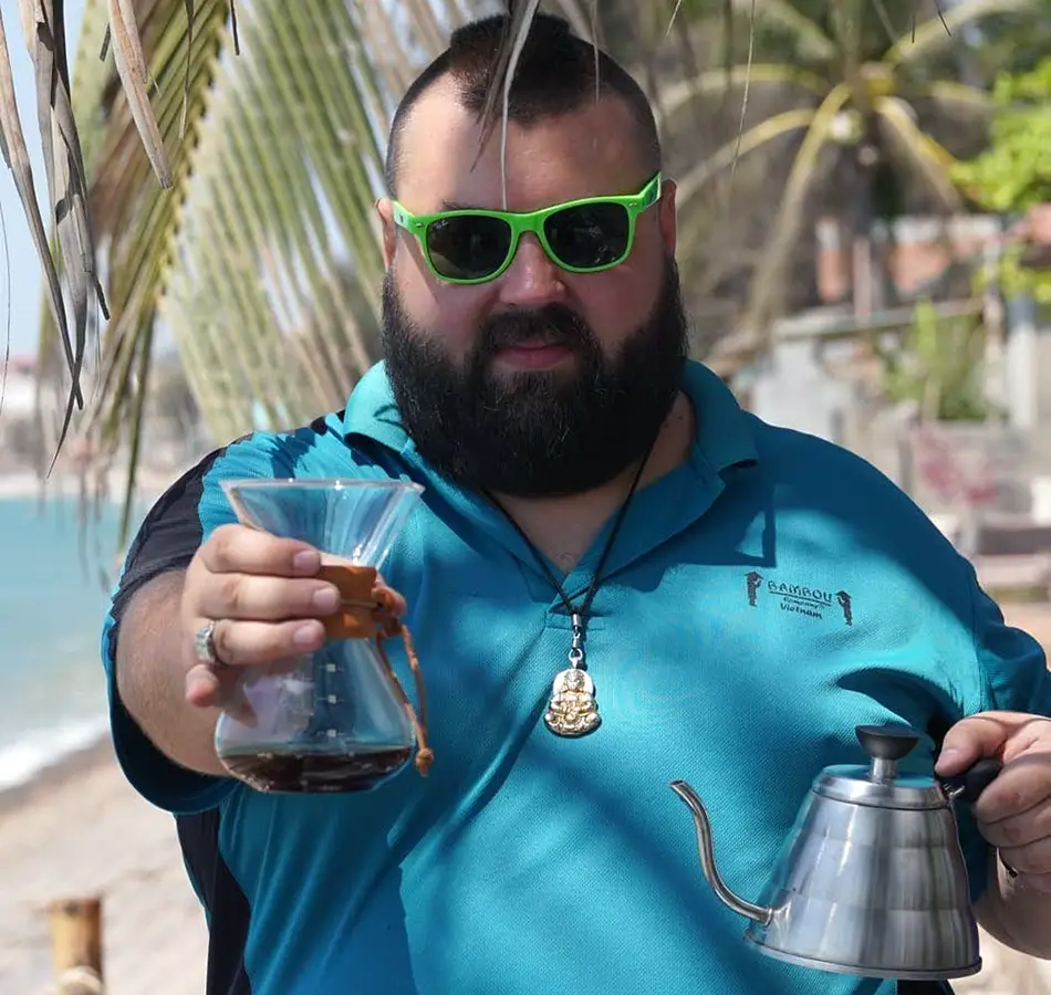 Restaurant owner holding drinks while standing near a tropical bar.