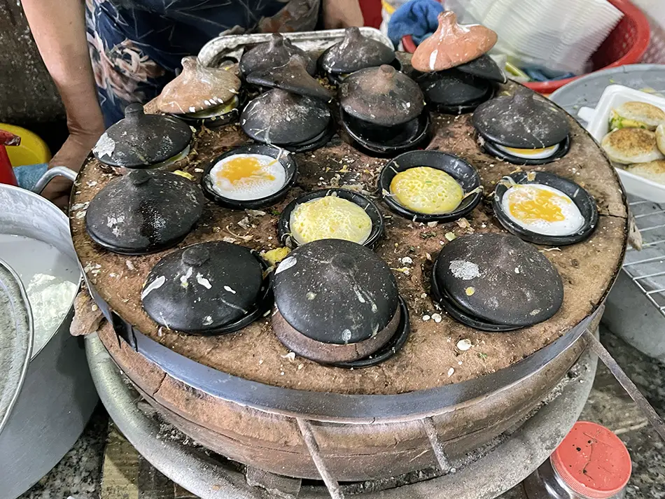 Clay pots cooking seafood pancakes at a busy market spot showing where to eat in Mui Ne.