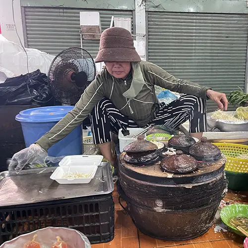 Vendor preparing dishes over charcoal stoves at a Mui Ne market stall.