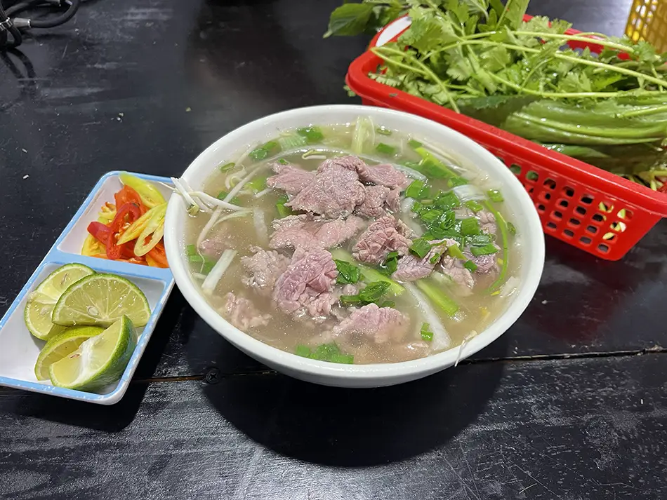 Steaming bowl of pho with herbs at Khue 259 - one of the Best Places to Eat in Mui Ne.
