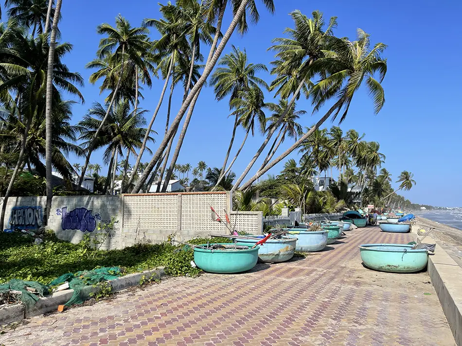 Palm-lined coastal promenade in Mui Ne with colorful fishing basket boats along the beach.