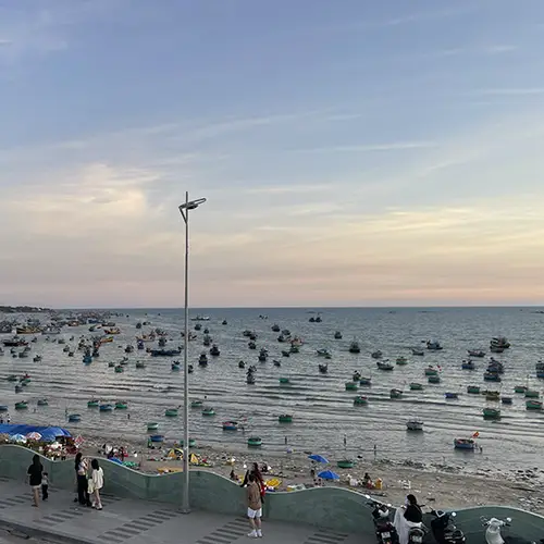 Panoramic view of Mui Ne fishing village at dusk, with dozens of colorful round coracle boats and fishing vessels crowding the harbor