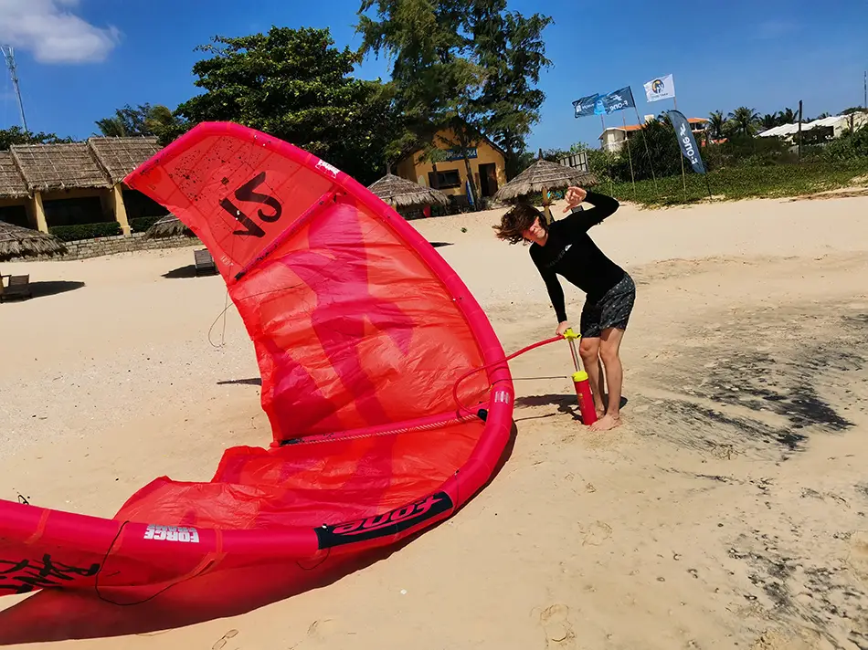 A kitesurfing student on a sandy beach in Mui Ne, with a large red kite laid out on the sand