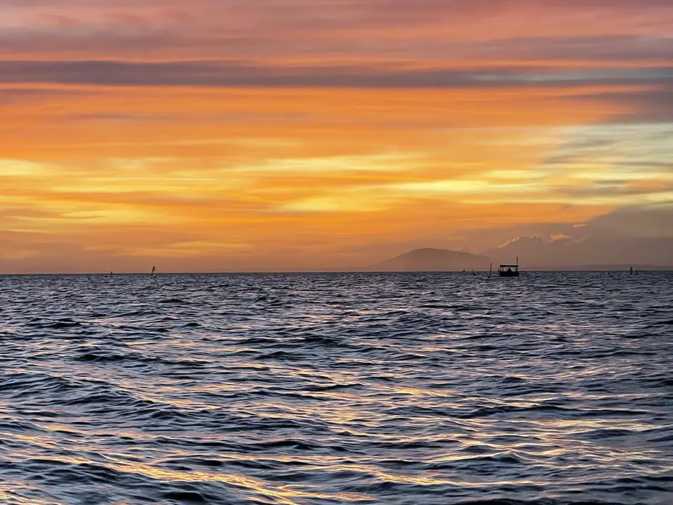 Dramatic Mui Ne sunset with deep orange, pink, and purple tones reflecting off the calm South China Sea, with a dark silhouette of the shoreline in the foreground