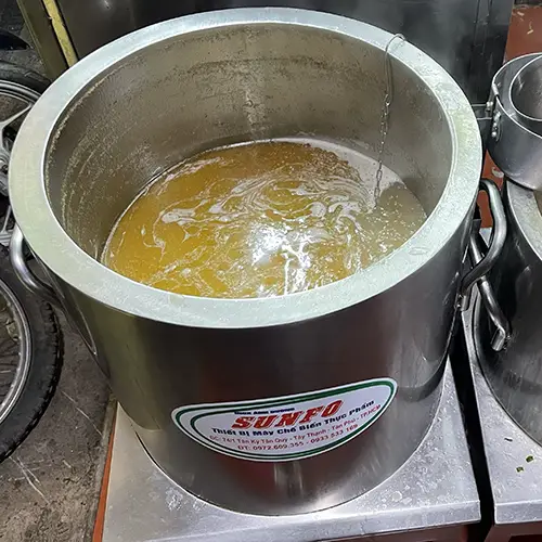 Metal pot of simmering broth on a portable stove beside fresh noodles.