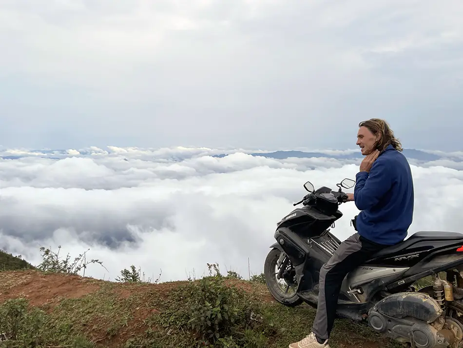 Traveler sitting on a motorbike at a Ta Xua viewpoint above a sea of clouds in northern Vietnam.