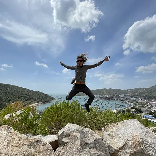 Traveler jumping on rocks at a viewpoint above Vinh Hy Bay.