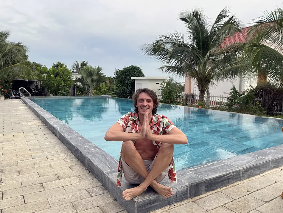 Traveler relaxing by a swimming pool at a Mui Ne beach hotel with palm trees and tropical resort setting.