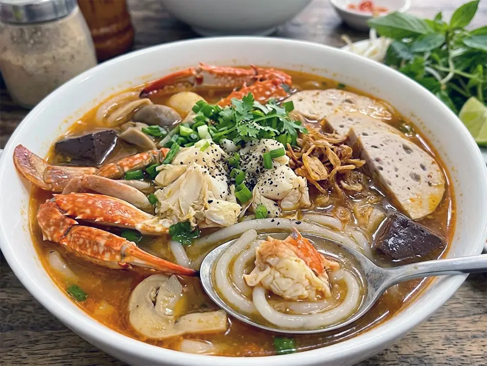 Bowl of bánh canh ghẹ crab noodle soup with thick tapioca noodles, blue swimmer crab, and fresh herbs