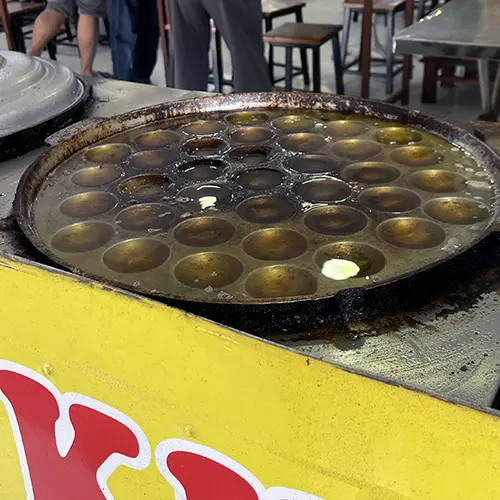 Bánh khọt batter being cooked in small cast-iron molds on a gas stove, showing the traditional preparation method
