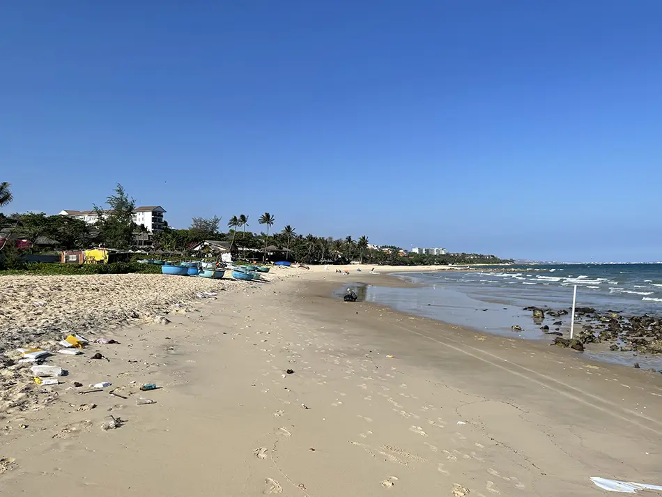 Plastic debris and litter scattered on an unmaintained section of sand between resort boundaries on the beache