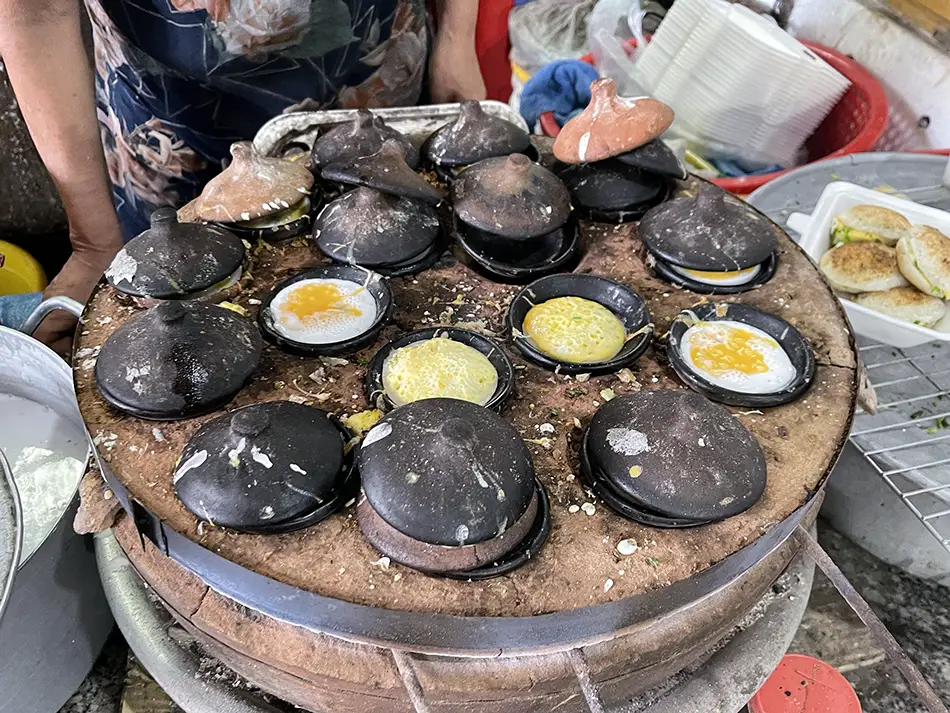 Overhead view of a round metal tray with small clay pots of cooked dishes at a local market stall in Ham Tien
