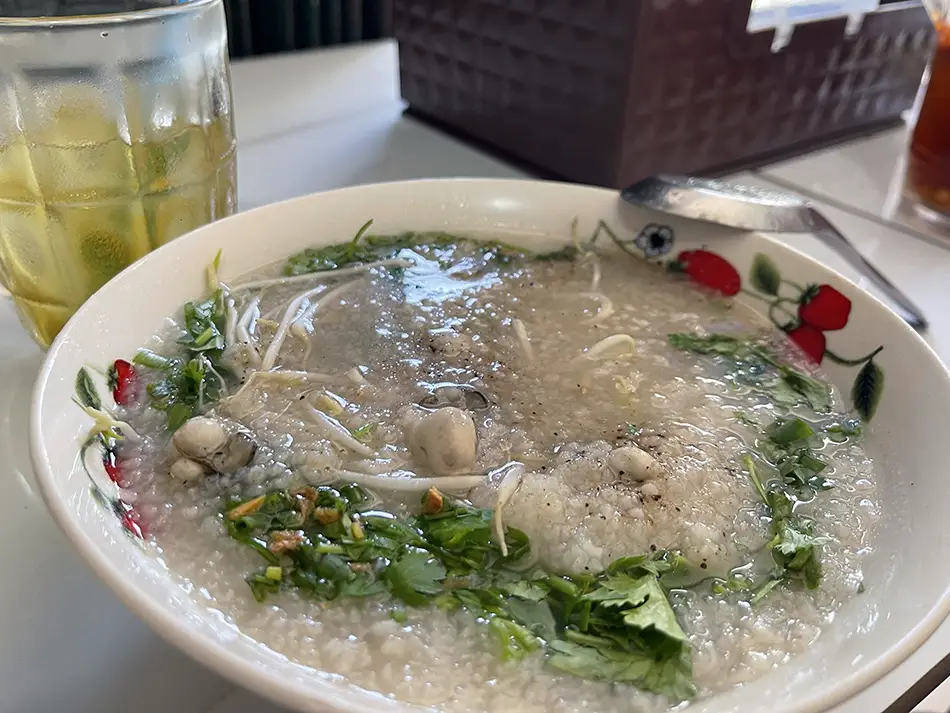 Bowl of cháo hàu oyster porridge topped with crispy shallots, green onion, and a drizzle of fish sauce