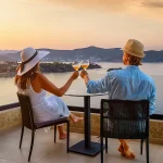 Couple enjoying wine tasting overlooking coastal landscape at sunset, representing wine travel experiences