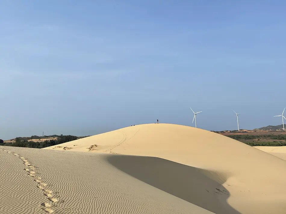 Rippled white sand dune ridge under a clear blue sky near Mui Ne, with footprints trailing along the crest