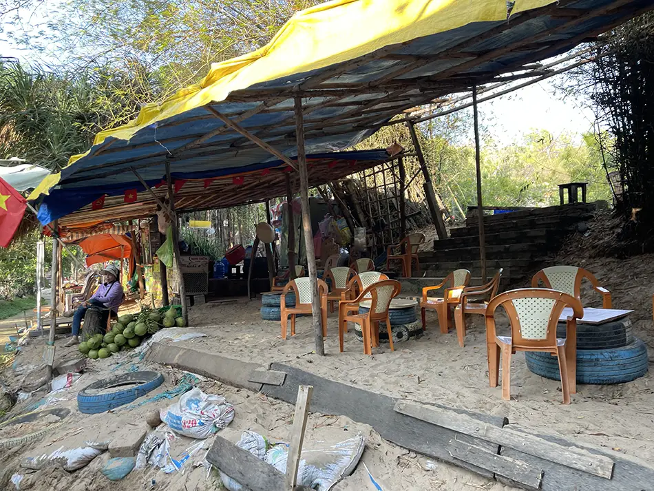 Open-air Vietnamese cafe stalls with plastic chairs and tables lining the early section of the Fairy Stream walk, shortly after the entrance stairs