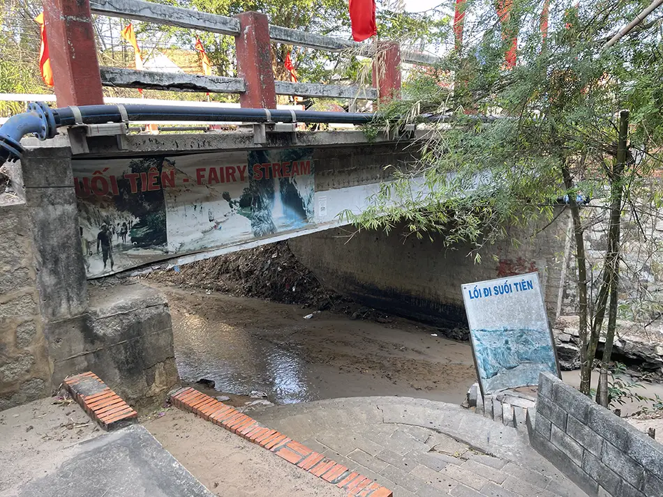 Concrete entrance stairs leading down to Fairy Stream in Mui Ne, with a bridge structure visible overhead